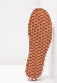 Sula för sko sedd från sidan, med ett diamantmönster i brunt gummi och vit kant. Platt design, lämplig för avslappnad användning.