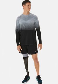 Pikad varrukad, halli ja musta tooniga spordipluus, mida kombineeritakse mustade lühikestega. Näha on proteesijalat ja sportlikke tossusid.