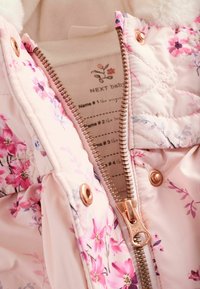 Hellrosa gesteppte Jacke mit Blumenmuster, ausgestattet mit einem goldenen Reißverschluss, Druckknopfverschlüssen und einem weichen Innenfutter. Markenschild ist innen sichtbar.