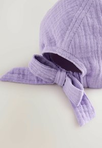 Lila Baumwollmütze mit strukturiertem Finish, ausgestattet mit einer gebundenen Schleife vorne und einem offenen Rücken für eine verstellbare Passform.