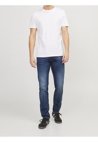 Vit bomulls-t-shirt som matchas med blå denimjeans. Jeansen har rak passform och en blekt tvätt. Svarta sneakers fulländar outfiten.