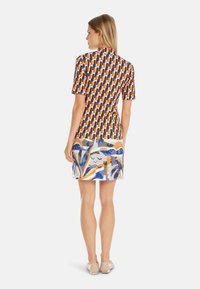 Bunt gemusterter Oberteil mit kurzen Ärmeln und figurbetonter Silhouette. Ein kontrastierender Rock mit abstrakten Designs in Blau, Orange und Grau.