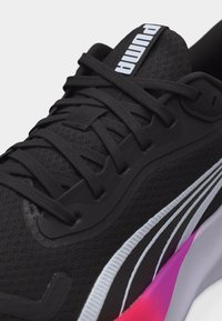 Κοντινό πλάνο μαύρου αθλητικού παπουτσιού Puma με μαύρα κορδόνια, υφασμάτινη υφή, λευκή ρίγα με το λογότυπο και λεπτομέρεια στη μεσαία σόλα με βαθμιδωτό ροζ προς μωβ χρώμα.