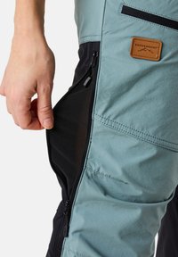 Vaaleansiniset ja mustat ulkoiluhousut, joissa on vetoketjullinen tasku; valmistettu teksturoidusta kankaasta. Nahkainen logo-painatus, jossa lukee "Swedemount."