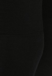 Leggings neri a coste realizzati in un materiale elastico, con una fascia in vita senza cuciture e una texture morbida. La vista ravvicinata mette in evidenza il tessuto.