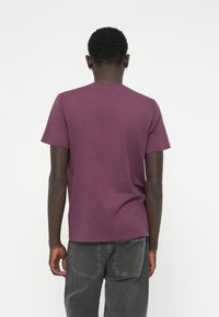 Tricou cu mânecă scurtă și guler rotund dintr-un material bordeaux închis. Croi clasic cu o textură netedă. Asortat cu pantaloni gri închis.