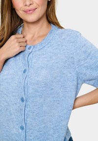 Jasnoniebieski, krótki kardigan z krótkim rękawem, wykonany z miękkiej dzianiny. Posiada okrągły dekolt, zapięcie na guziki z przodu oraz subtelną teksturę z dopasowanymi guzikami.