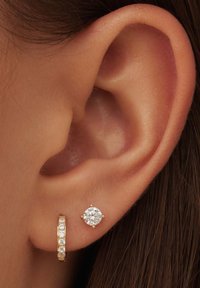 Goldfarbene Ohrringe mit einem Ohrstecker, der einen klaren runden Edelstein besitzt, kombiniert mit einem dünnen Creolenring, der mit kleinen klaren Steinen besetzt ist.
