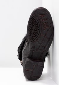 Sort læderstøvle med synlige slidmønstre på sålen, en lynlås i siden og pelskant omkring anklen, vist mod en hvid baggrund.