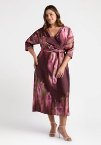 Wickelkleid aus dunkelburgunderfarbener Stoff mit rosa Blumenmuster. Es hat Dreiviertelärmel, einen Gürtel in der Taille und einen V-Ausschnitt.