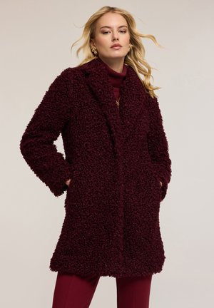 Bordeaux fuzzy jas met een textuur oppervlak, notch revers en zijzakken. Gedragen over een bijpassende coltrui en broek.