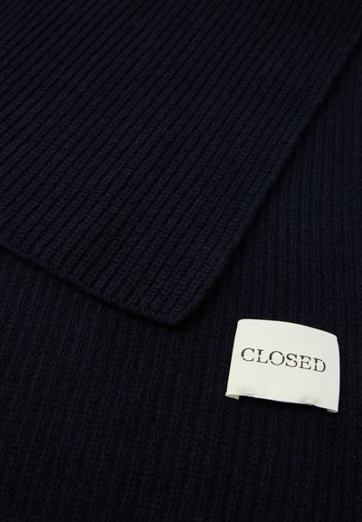 Tmavomodrý rebrový pletený materiál s bielou obdĺžnikovou nálepkou, na ktorej sú v horných písmenách napísané slová "CLOSED".