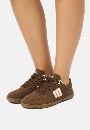 Zapatillas de ante marrón con cordones marrones, que cuentan con un logo crema y suela de goma. Textura suave y diseño de perfil bajo.