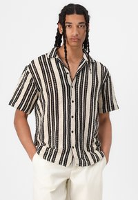 Camisa de manga corta con botones y textura de punto, con rayas alternas en negro y crema, cuello con muesca y cierre frontal con botones.