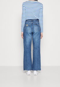 Džíny s vysokým pasem, široké nohavice, modré denimové s třepícími se lemy. V módní kombinaci s dlouhým pruhovaným tričkem. Na nohou bílé tenisky.