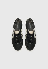 Sneakers feature a black mesh upper with beige accents and a textured sole. Designed with multiple ventilation holes and round laces.