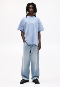Light blue cotton t-shirt with "Atlanta, Georgia" text, paired with loose-fitting light blue denim jeans and black shoes.