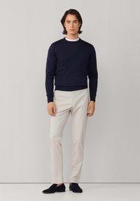 Marineblauwe sweatshirt met geribbelde boorden en zoom, gecombineerd met lichte broek. Model staat met handen langs het lichaam en draagt donkere schoenen.