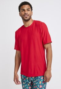 Czerwona koszulka z krótkim rękawem, wykonana z lekkiego materiału o gładkiej fakturze. Posiada klasyczny okrągły dekolt i luźny krój. W zestawie z wzorzystymi szortami.