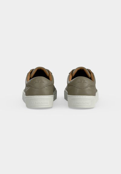 Paire de baskets vert olive avec semelles blanches vues de dos sur un fond gris uni.