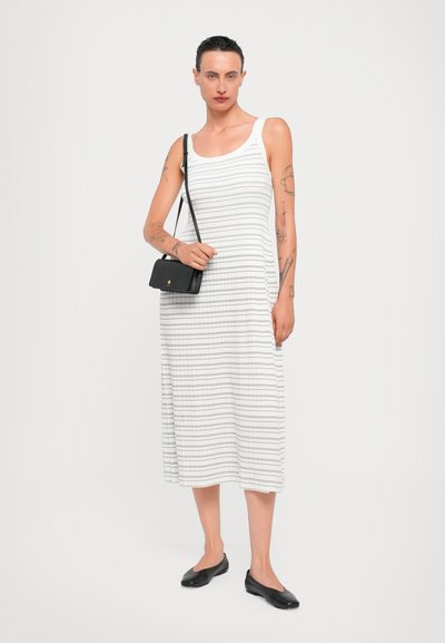 Weißes ärmelloses Kleid mit schwarzen horizontalen Streifen, knielang. Kombiniert mit einer kleinen schwarzen Handtasche und schwarzen Ballerinas.