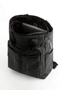 Svart, mjukt tyg ryggsäck med dragkedja, yttre fickor och ett mönstrat inre. Rymmer en laptop med vadderade sektioner för skydd.