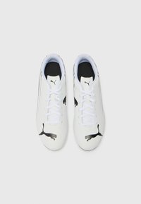 Des chaussures de sport blanches avec des accents noirs et des rayures audacieuses, arborant un logo Puma noir bien visible et des lacets blancs sur une surface texturée.