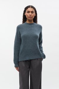 Maglione color teal, in morbido maglione lavorato a maglia, con collo alto, maniche lunghe e vestibilità comoda, abbinato a pantaloni scuri a righe sottili.