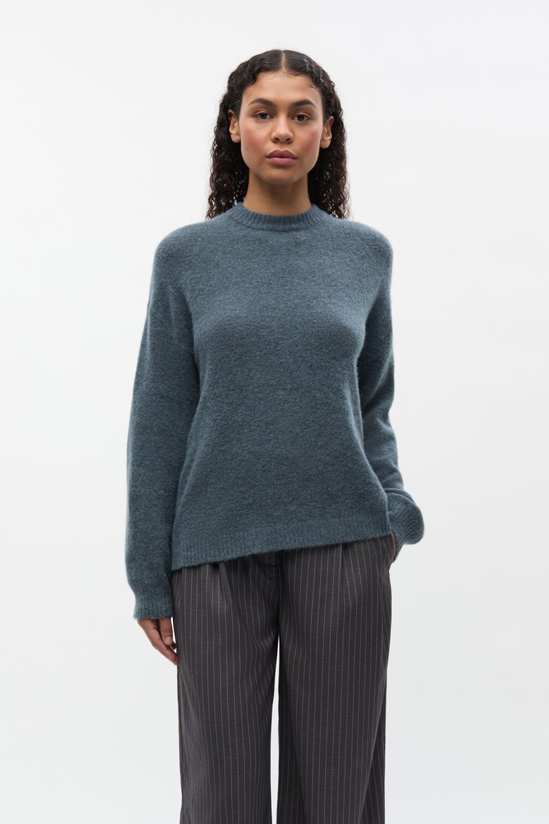 Maglione color teal, in morbido maglione lavorato a maglia, con collo alto, maniche lunghe e vestibilità comoda, abbinato a pantaloni scuri a righe sottili.