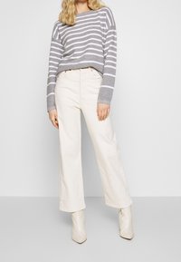 Grijs en wit gestreepte cropped trui, wijde crèmekleurige broeken en puntige witte enkellaarsjes. Zacht materiaal, casual pasvorm, minimale details.