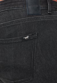 Svart jeans i denim med smal passform, med en läderlapp märkt "MUSTANG" och en liten broderad hästlogotyp på bakfickan.