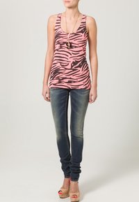 Débardeur rose avec des rayures zèbres noires, accompagné de jeans skinny décolorés. Les accessoires incluent un long collier pendentif et des sandales à plateforme beige.