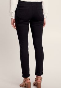 Jean skinny noir à taille haute, avec des poches arrière et un ourlet retroussé. Le tissu a l'air extensible et lisse.