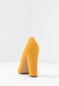 Chaussure à talon haut jaune avec une surface texturée ressemblant à du cuir de serpent, bout arrondi et talon large et épais.