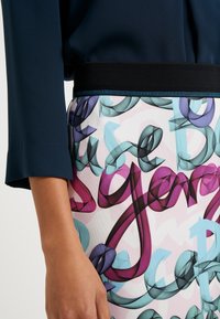 Blouse marine à manches retroussées et ceinture noire, associée à une jupe colorée présentant des formes abstraites et fluides en rose, violet et bleu.