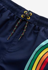 Námořní plavky s multicolor duhovým proužkovaným vzorem, s pletenou šnúrkou s žlutými akcentmi. Hladký, jemný materiál.