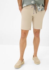 Shorts khaki con una texture liscia, dotati di tasche anteriori, passanti per cintura e un sottile accento con cordoncino. Abbinati a scarpe beige slip-on.