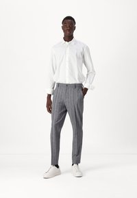 Bjela košulja s dugim rukavima, sivi hlače s prugama, i bijele tenisice; slim-fit dizajn, glatka tekstura i krojeni detalji.