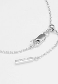 Bracciale in argento con chiusura a moschettone, dal texture liscia, e un charm cilindrico con dettaglio inciso. I link della catena sono delicati.