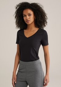 Sort kortærmet t-shirt med v-hals design, lavet af blødt stof, parret med grå højtaljede bukser. Simpelt og alsidigt outfit.