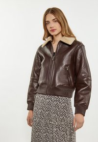 Giubbotto bomber in pelle marrone con colletto in shearling beige, polsini e orlo a coste, con zip frontale e tasca laterale.