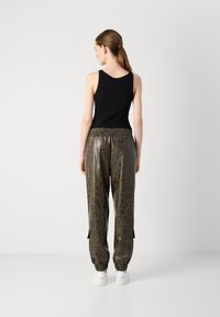 Musta hihaton paita yhdistettynä oliivinvihreisiin, kuviollisiin jogginghousuihin, joissa on kiiltävä pinta ja joustava vyötärö, sekä valkoiset tennarit.