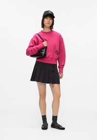 Felpa corta fucsia con logo, gonna nera plissè con dettaglio in pizzo, borsa nera, calze grigie e ballerine nere.