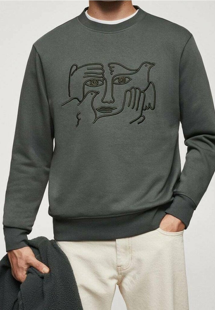 Bluza z okrągłym dekoltem z abstrakcyjną grafiką liniową przedstawiającą twarz i dwa ptaki, noszona przez osobę trzymającą ciemną kurtkę i ubraną w jasne spodnie.