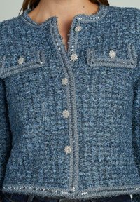 Giacca in tweed blu a trama, con design corto, caratterizzata da dettagli in paillettes argento, chiusura con bottoni e tasche a patta.