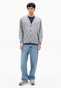 Cardigan gris avec un col en V, cinq boutons et des poignets côtelés sur une chemise bleue. Assortis à un jean bleu clair ample et des baskets grises.