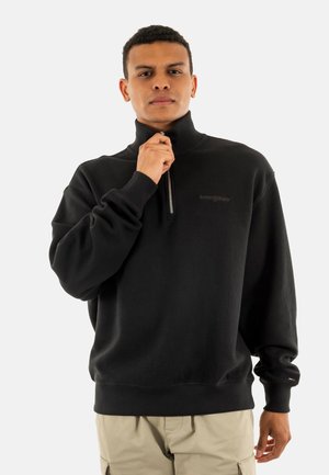 Sudadera negra de cuello alto, con cierre de media cremallera y tejido texturizado. Presenta un logo en el pecho y puños acanalados.