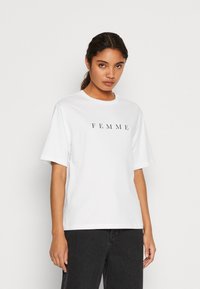 Witte katoenen T-shirt met korte mouwen en een ronde hals, met "FEMME" in het zwart op de borst gedrukt. Eenvoudige en relaxte pasvorm.