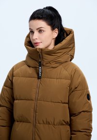 Bruine pufferjack met een hoge kraag, horizontale quilting en zijzak. Rits aan de voorkant met een merkachtige trekker en zwarte accenten.