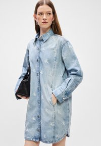 Heledasinine denim kleit krae, nööbid ees, pikad varrukad, küljetaskud ja CK logo muster üle kogu kleidi.